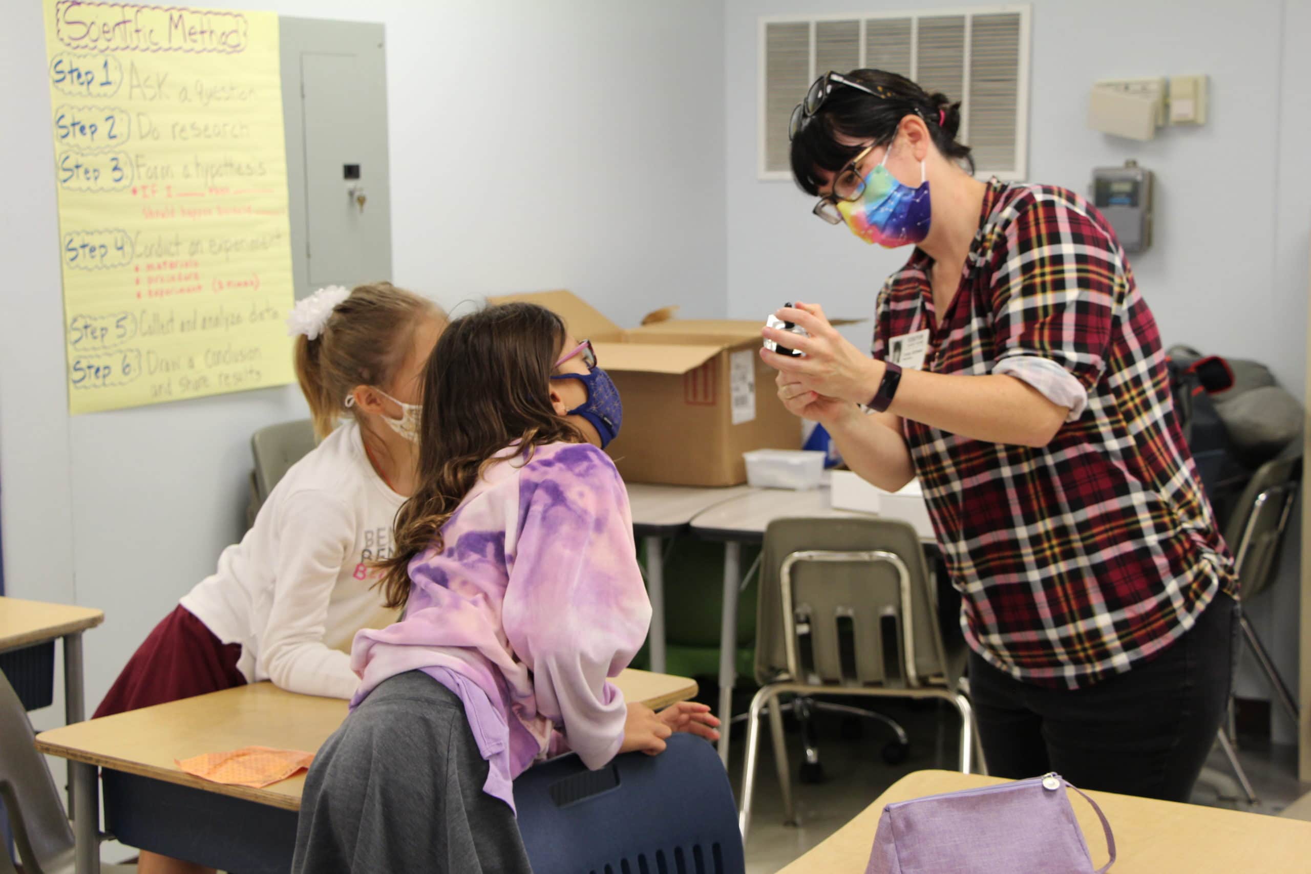 Woman demonstrates a science lesson to two young students in classroom